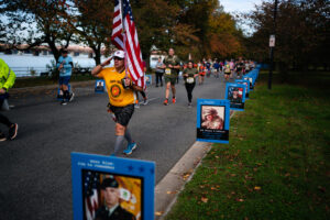 A man carrying an American Flag salutes a poster of a deceased service member.